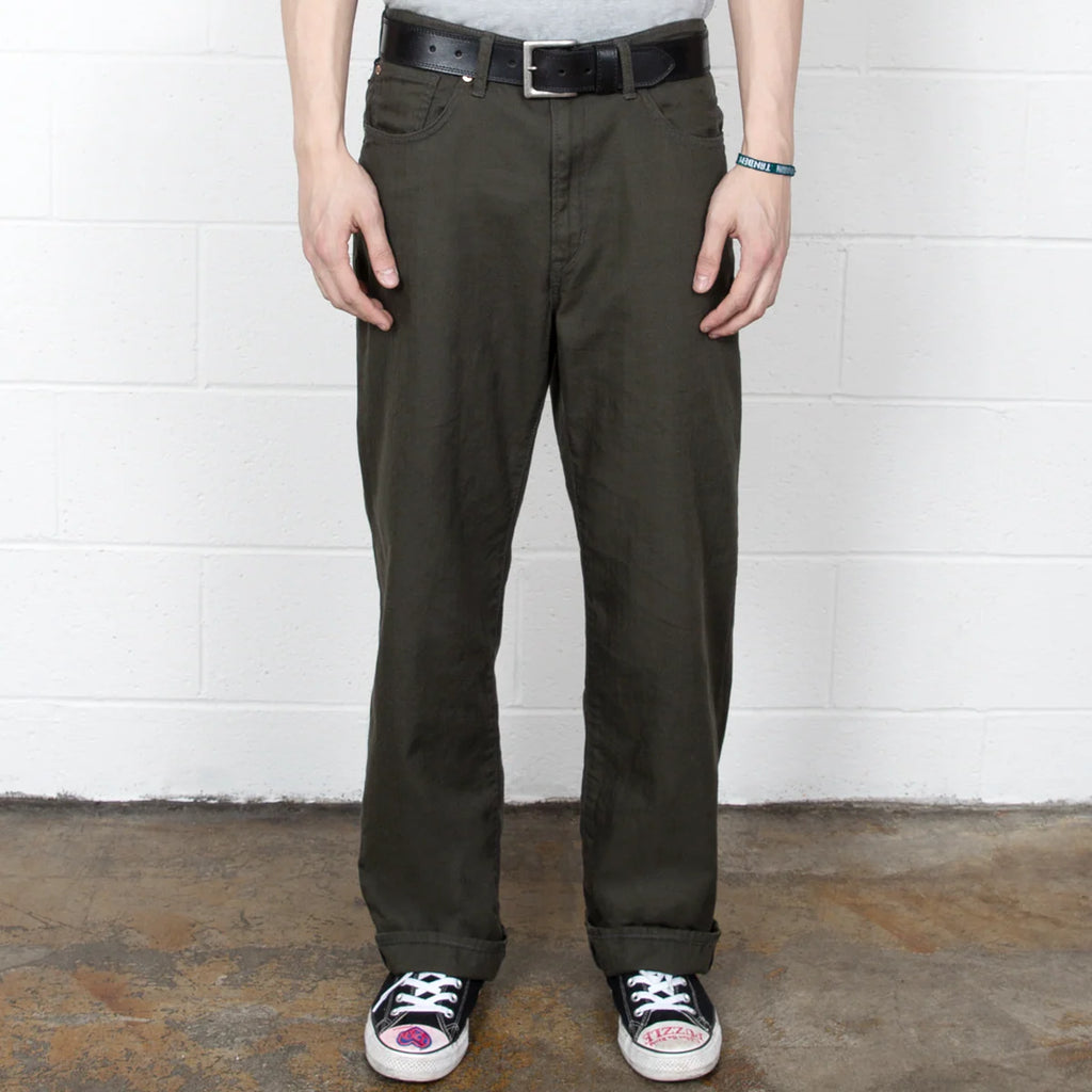 Person wearing dark green pants and black sneakers against a white wall.