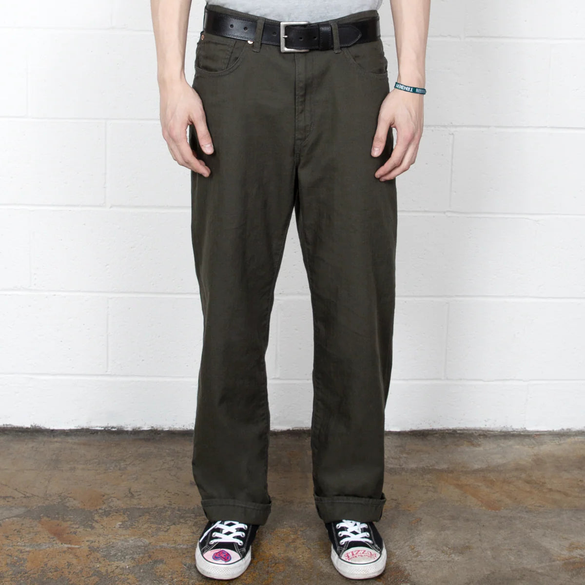 Person wearing dark green pants and black sneakers against a white wall.