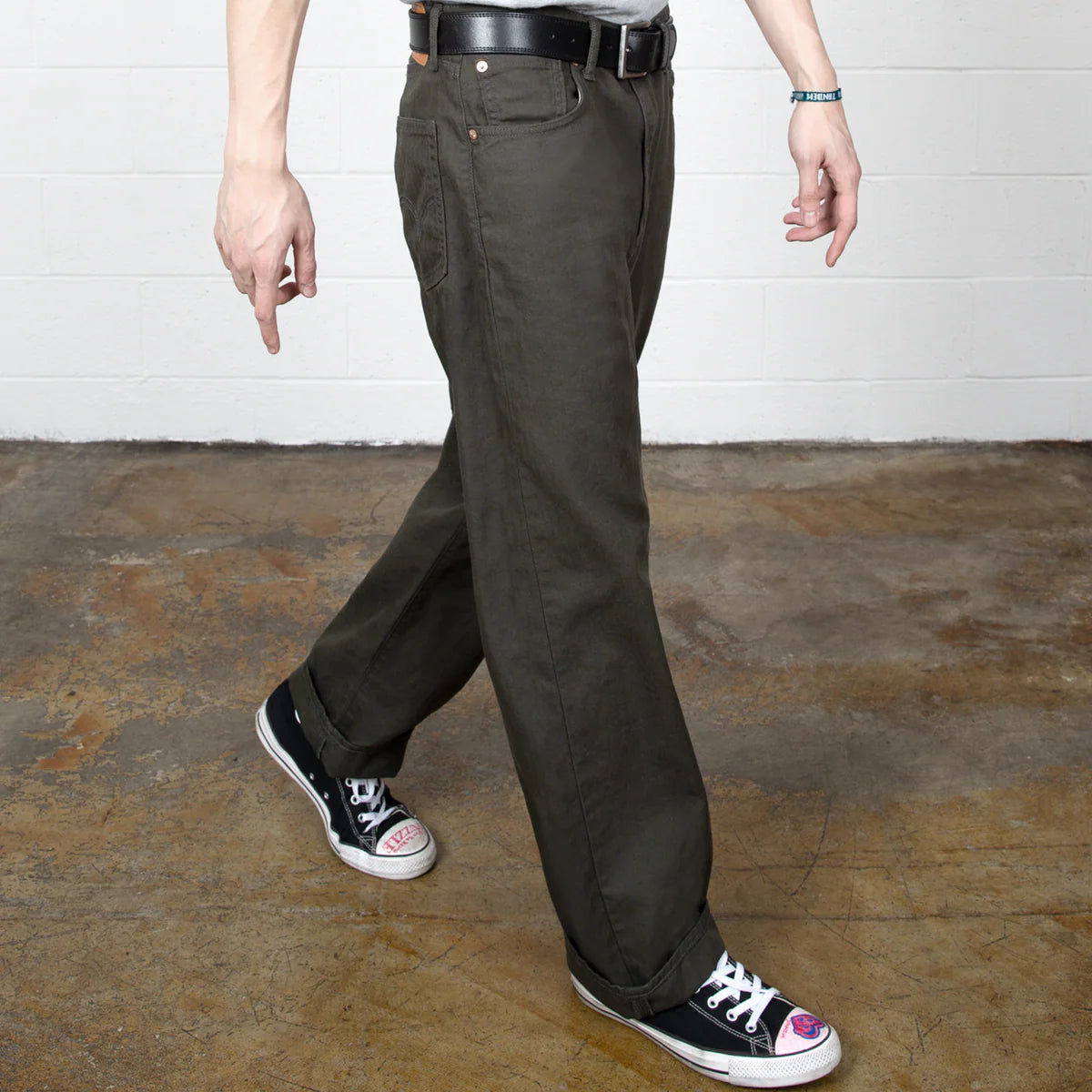 Person wearing dark green pants and black sneakers in a room with a white wall and wooden floor.