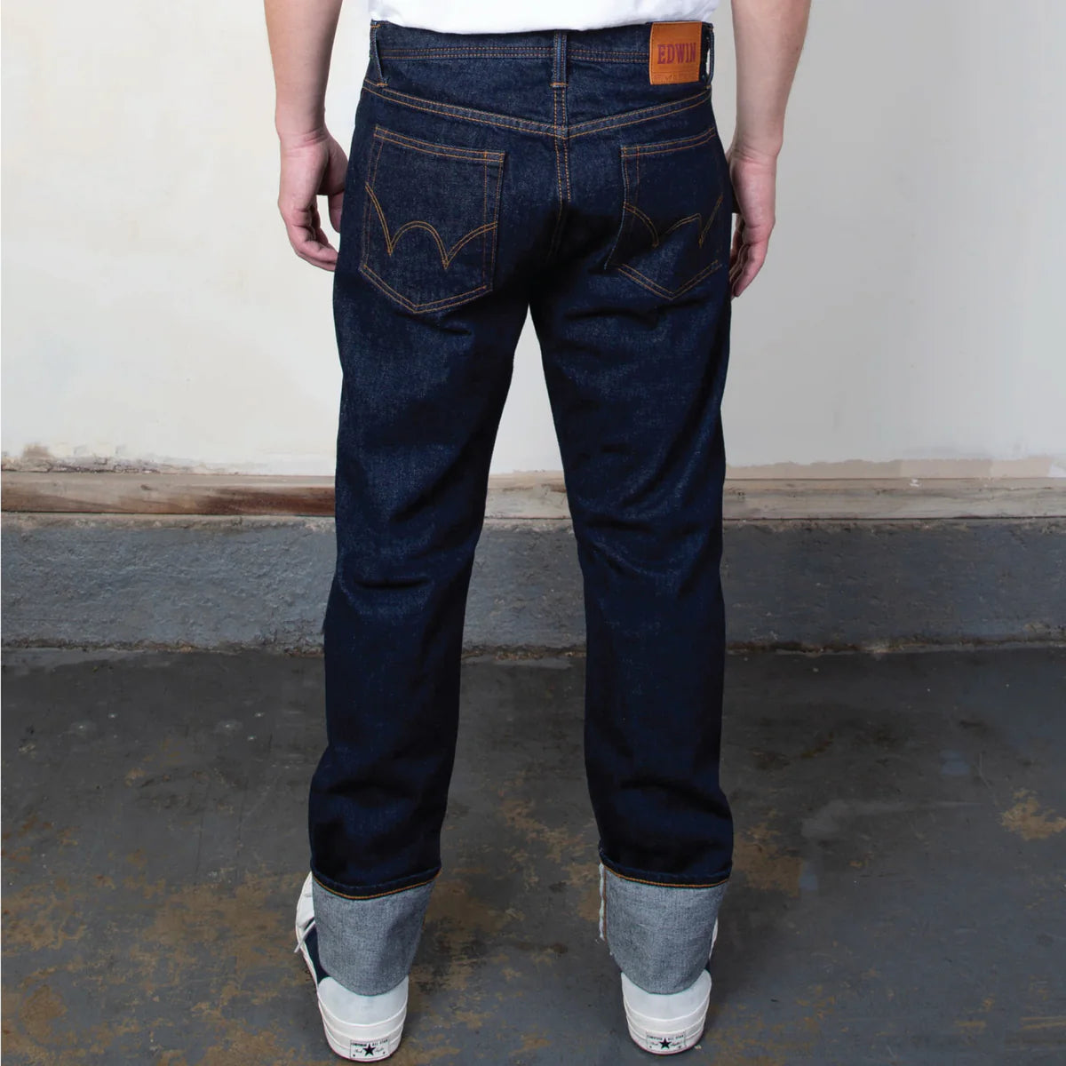 Person wearing dark blue jeans with a plain background