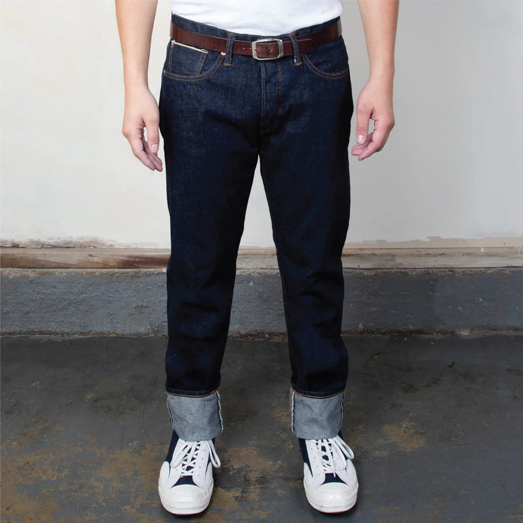 Person wearing dark blue jeans with white sneakers on a plain background