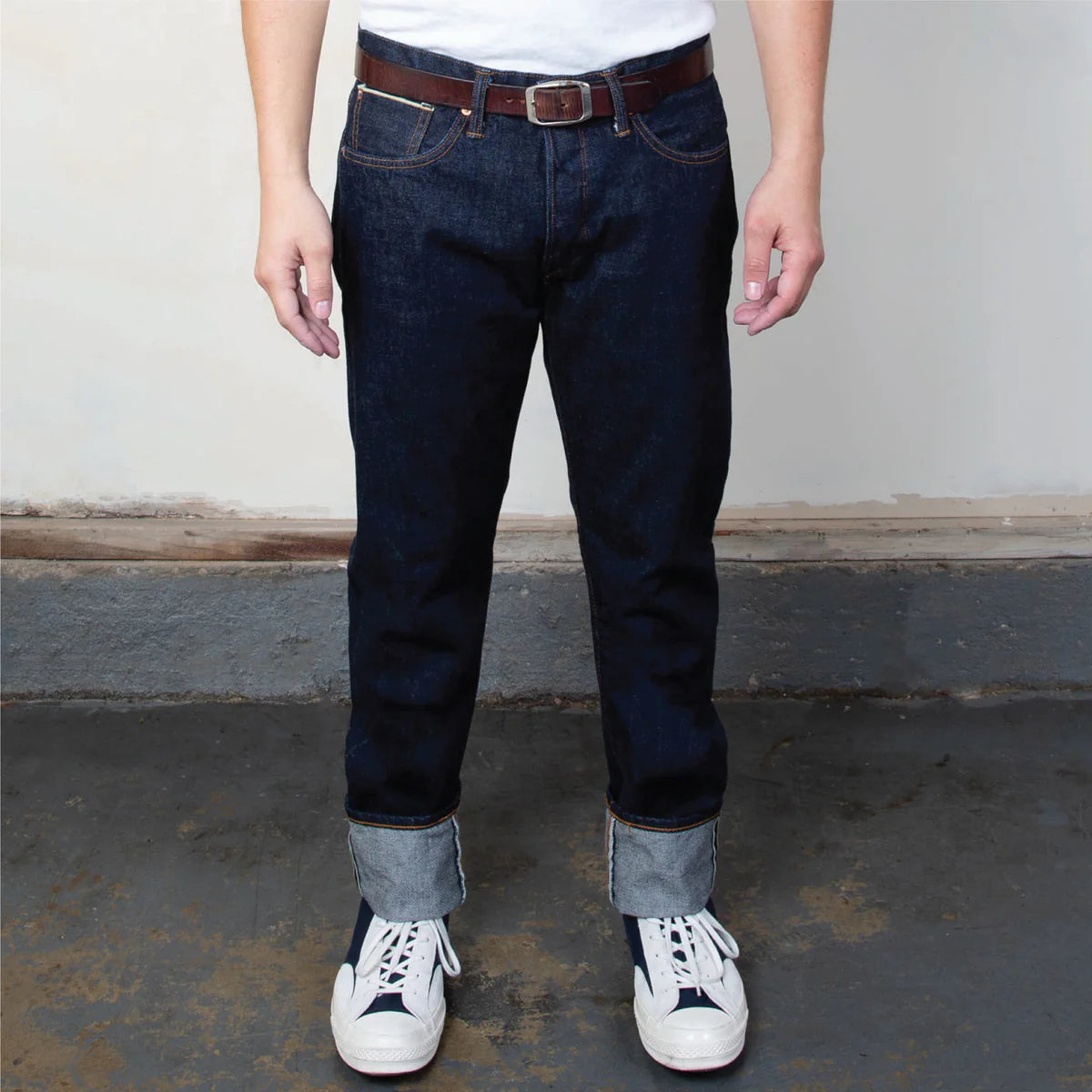 Person wearing dark blue jeans with white sneakers on a plain background
