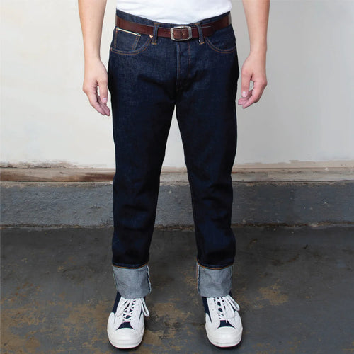 Person wearing dark blue jeans with white sneakers on a plain background