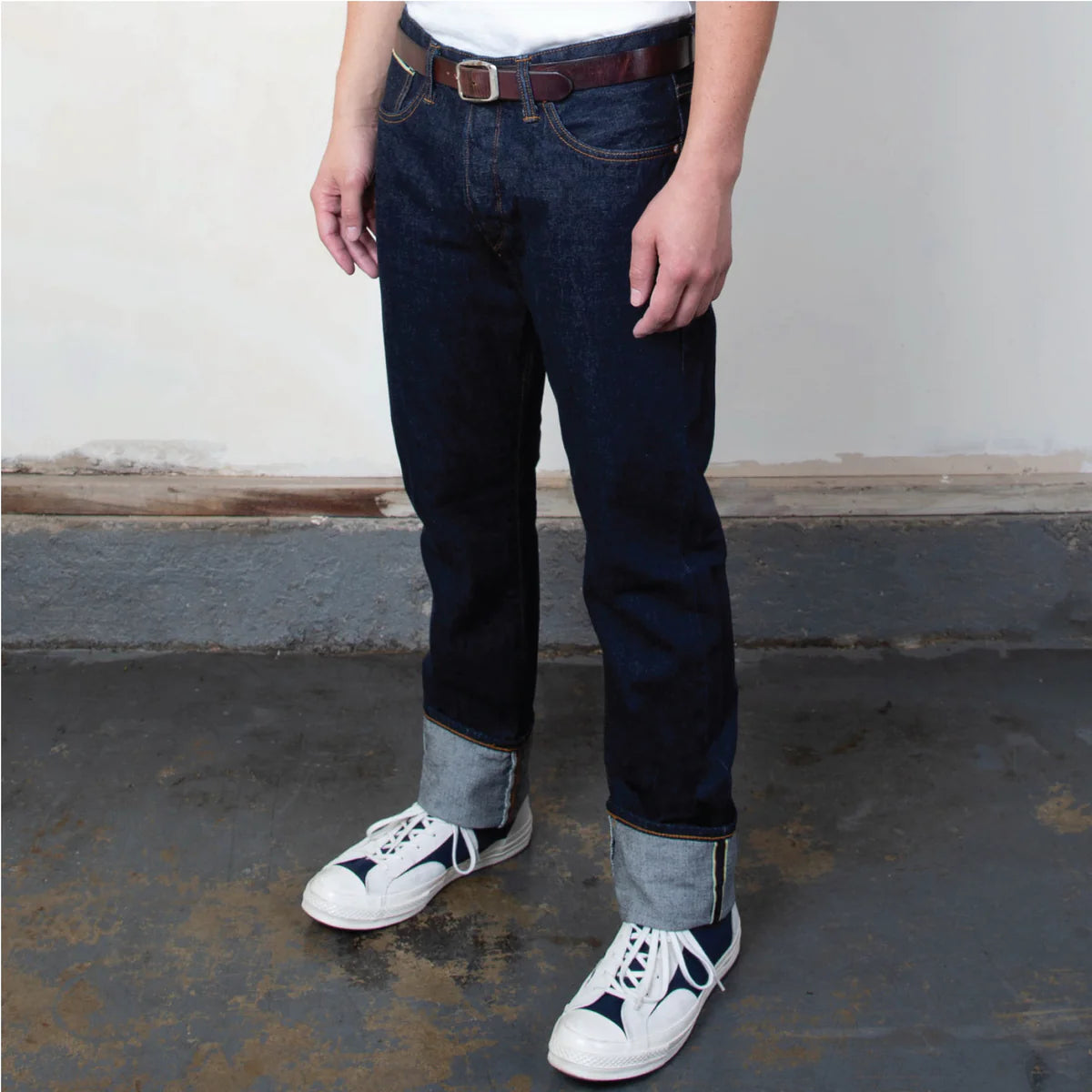 Person wearing dark blue jeans and white sneakers with black accents on a concrete floor.