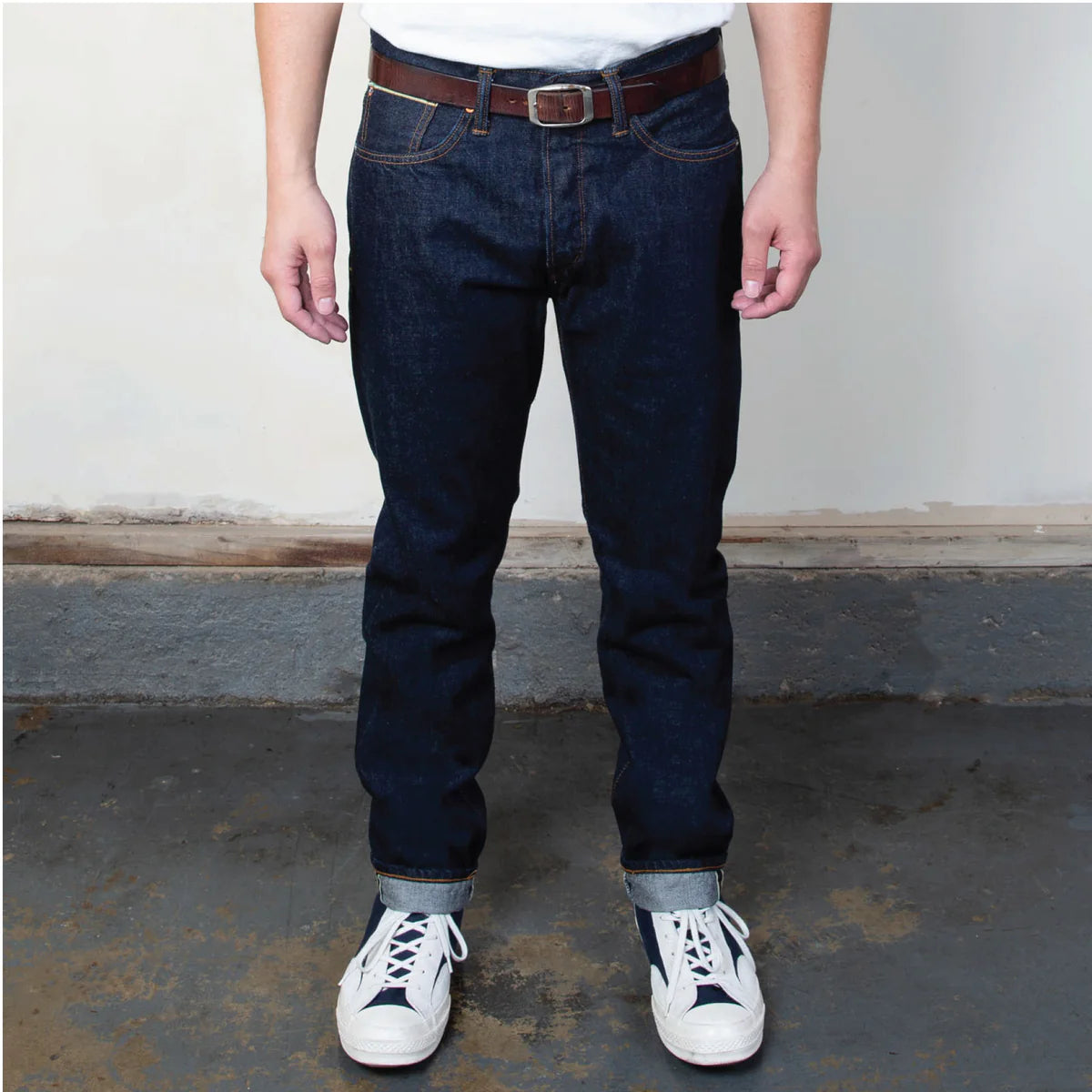 Person wearing dark blue jeans and white sneakers on a plain background