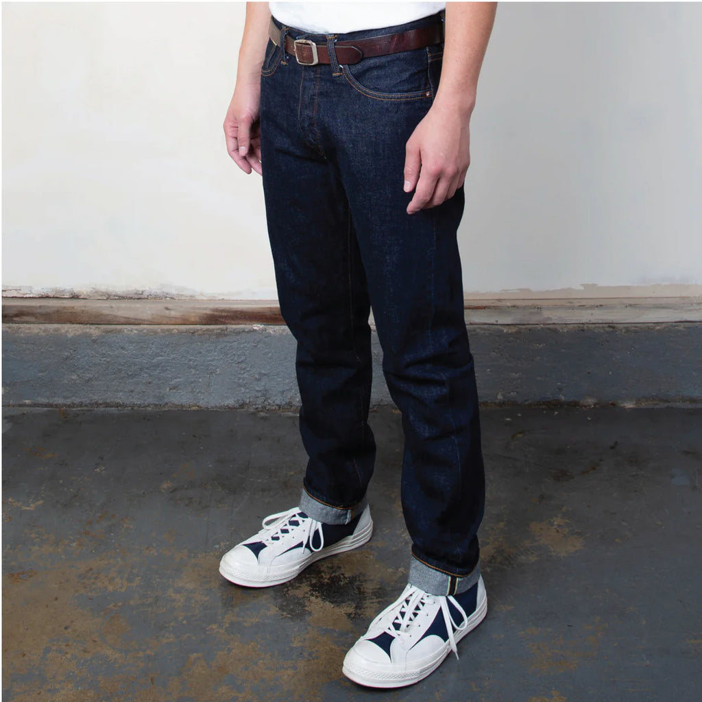Person wearing dark blue jeans and white sneakers on a concrete floor.