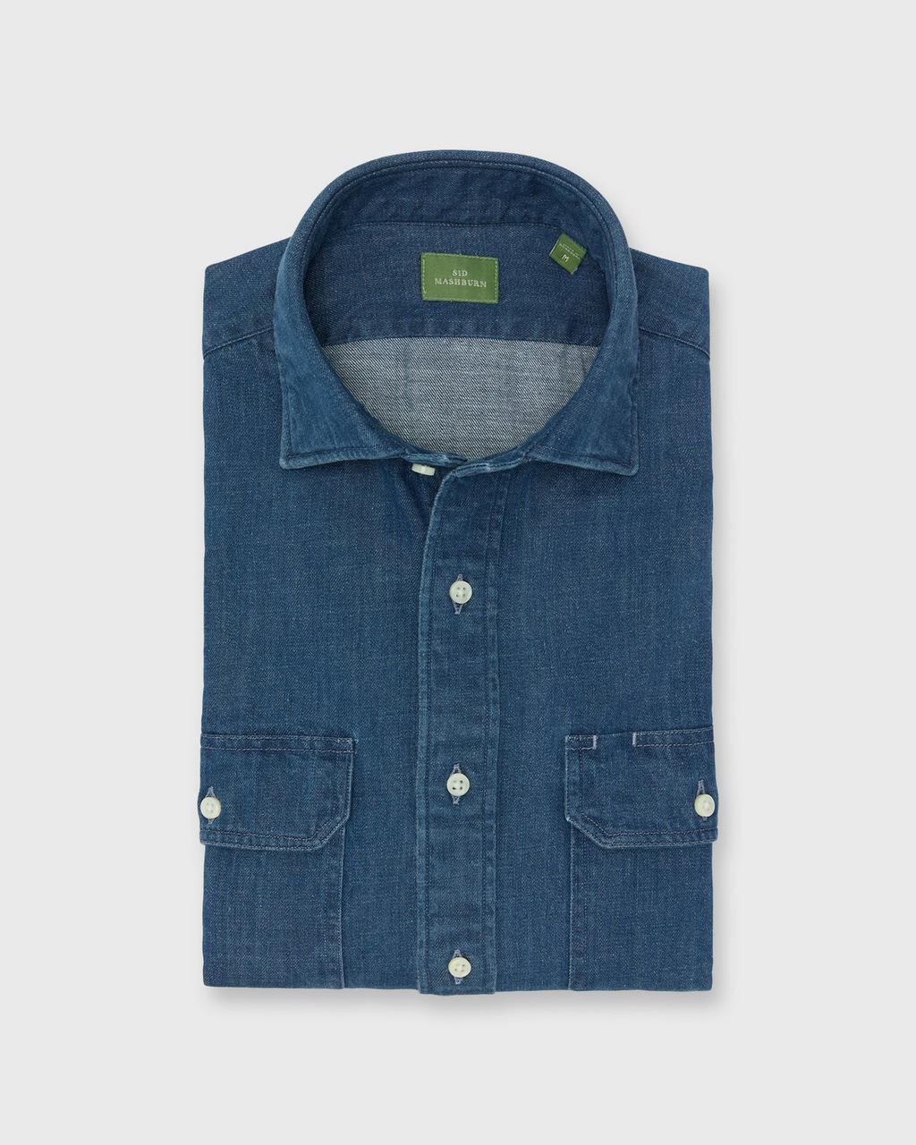 Blue denim shirt with a green label on a light gray background