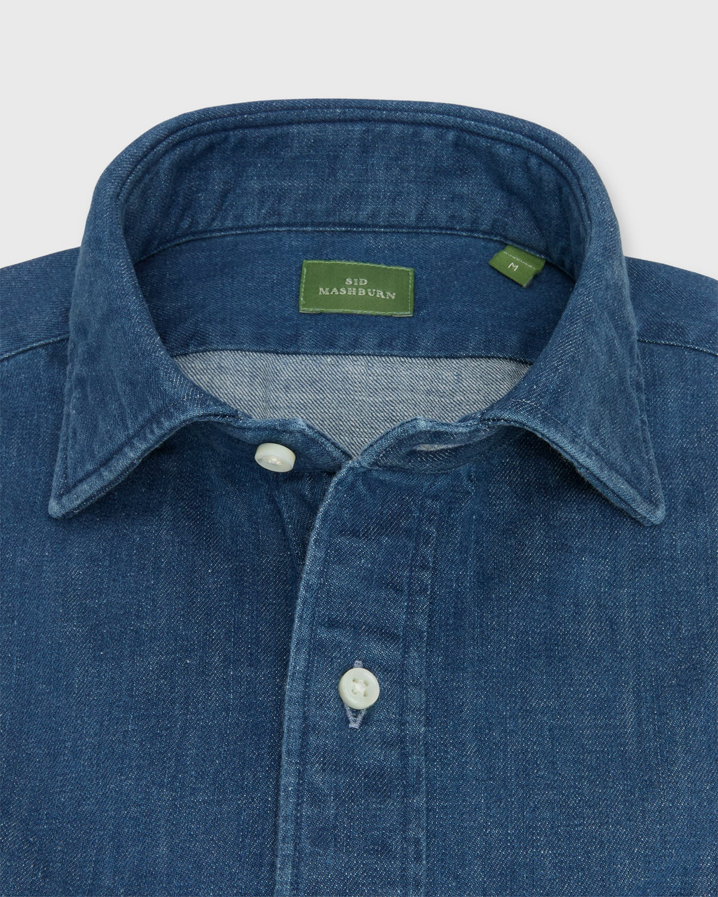 Close-up of a blue denim shirt with a brand label on a light gray background