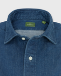 Close-up of a blue denim shirt with a brand label on a light gray background