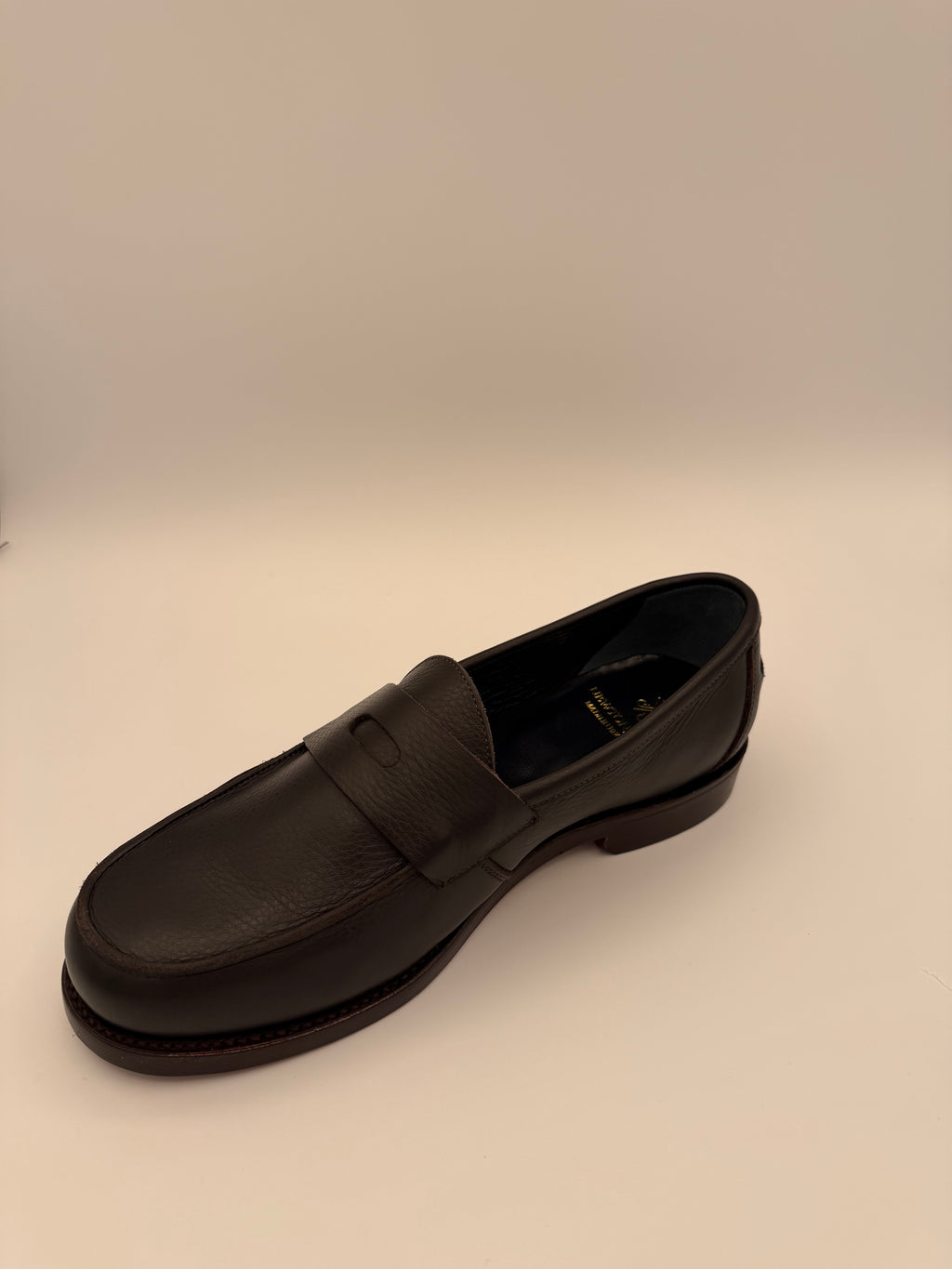 side view of Black leather shoe on a beige background