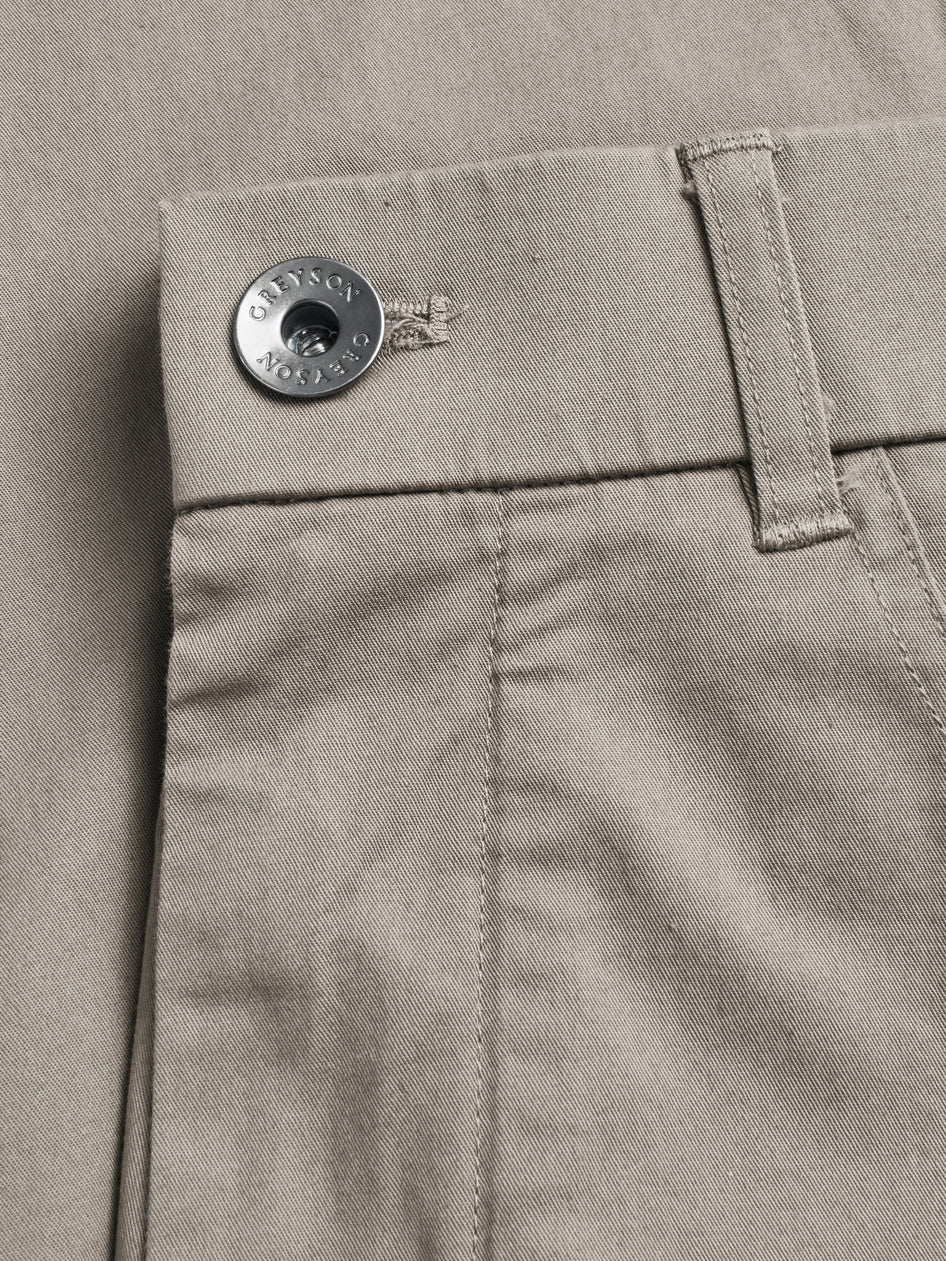 Close-up of a button on a beige pants pocket with a brand logo.