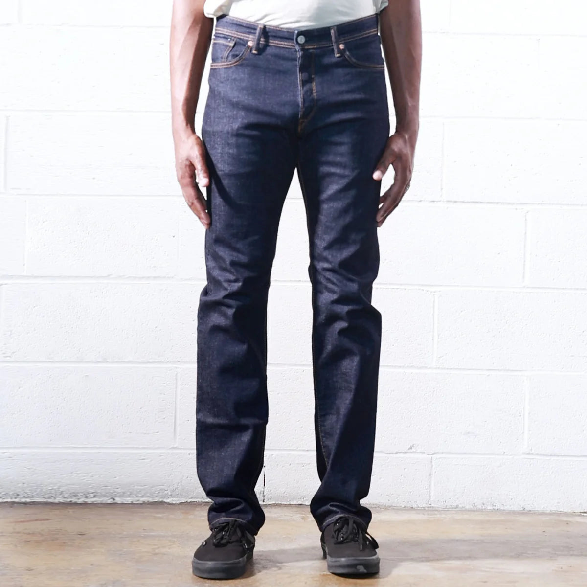 Person wearing dark blue jeans against a white brick wall.
