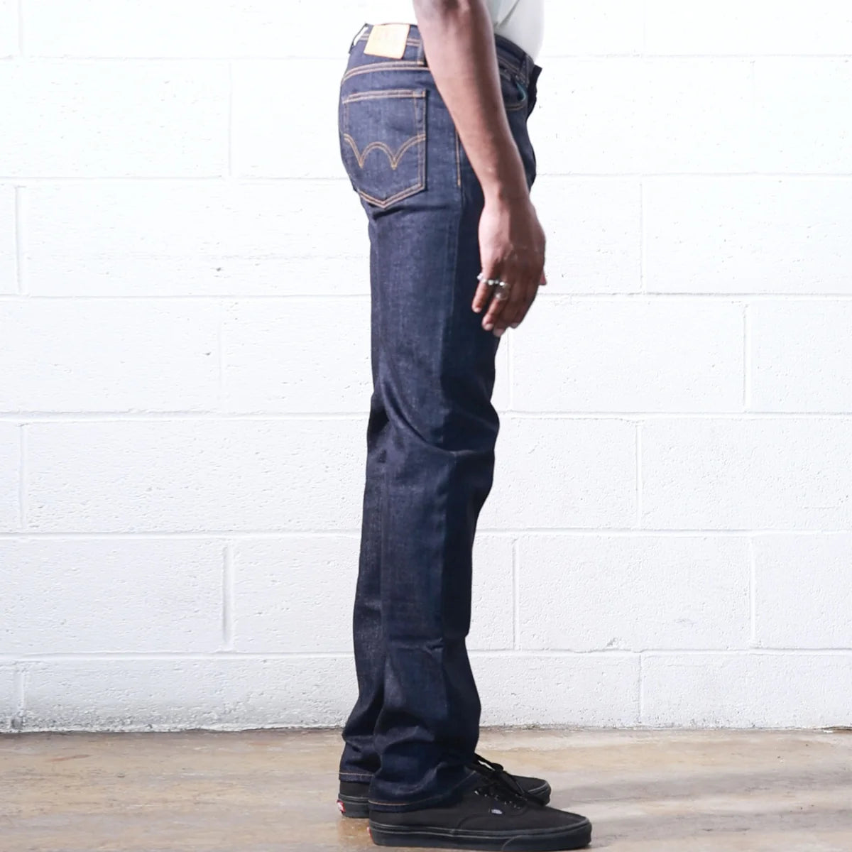 Person wearing dark blue jeans standing against a white brick wall.