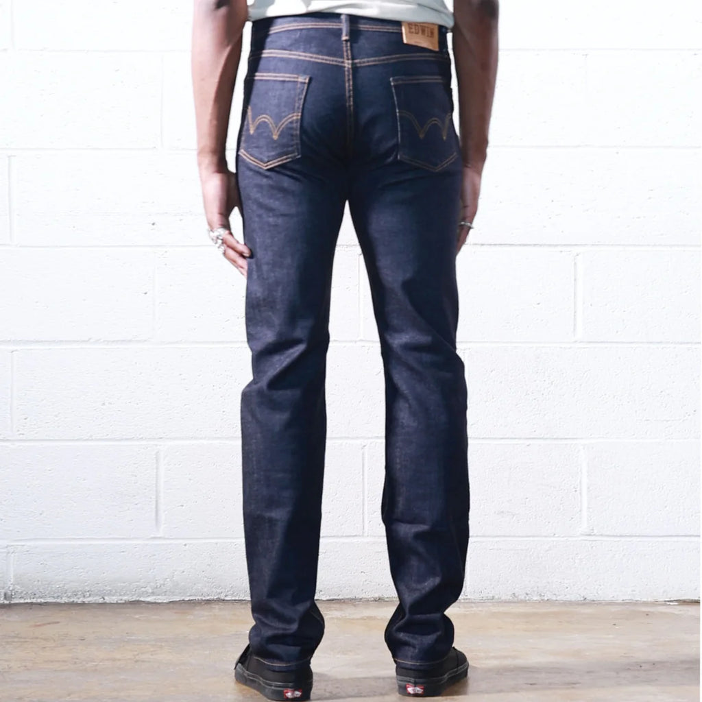 Person wearing dark blue jeans with a visible brand logo against a white brick wall.