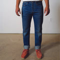 Person wearing blue jeans and red shoes standing on a concrete floor with a white wall background.