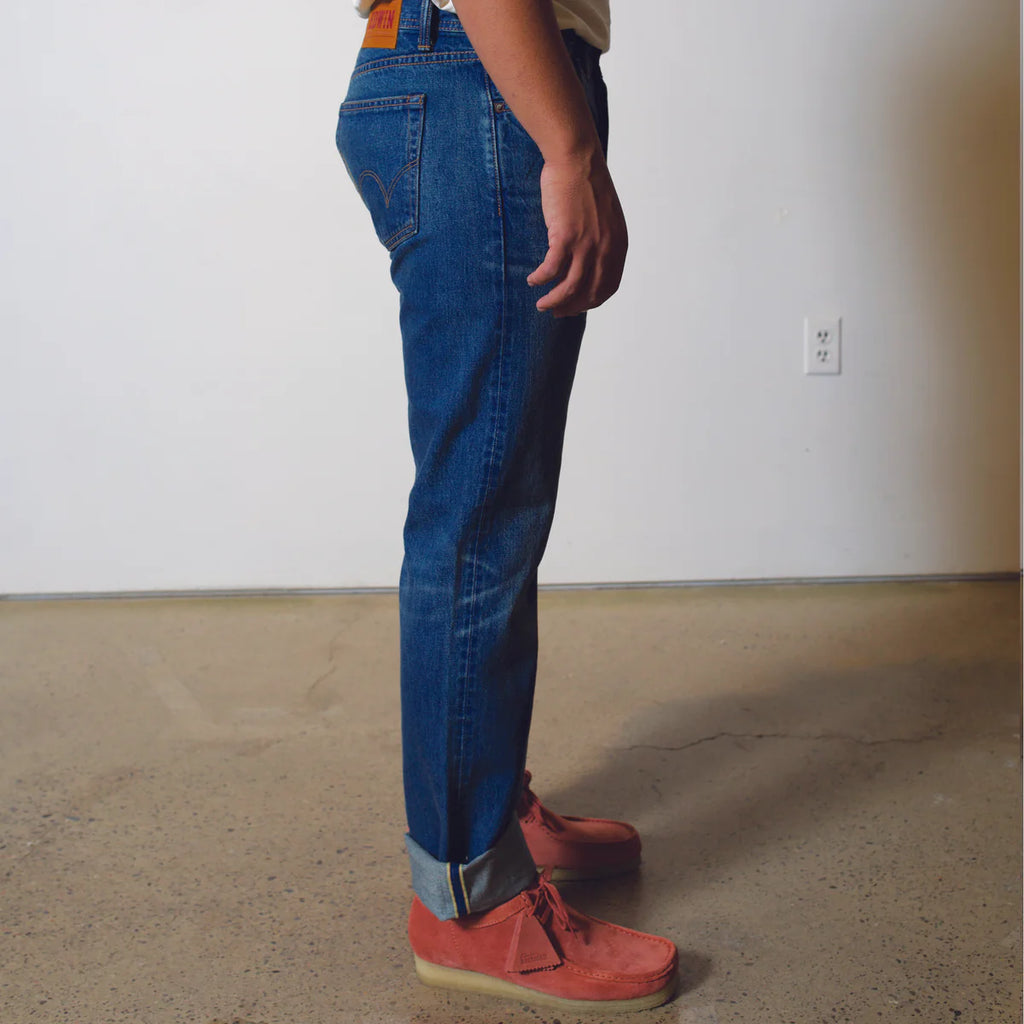 Person wearing blue jeans and red shoes standing in a room with a plain wall and floor.