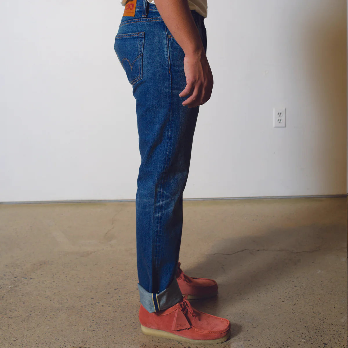 Person wearing blue jeans and red shoes standing in a room with a plain wall and floor.